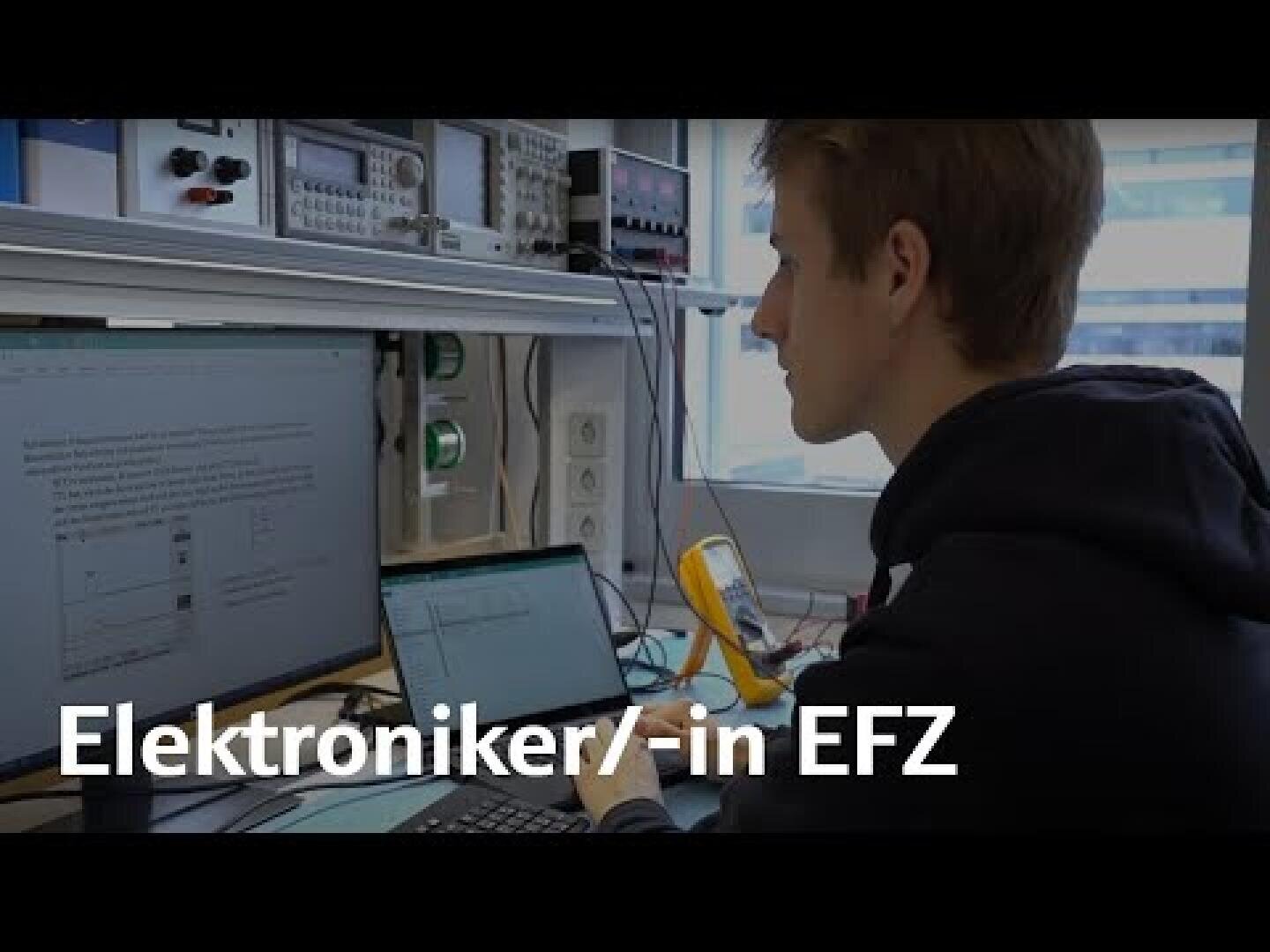 Eine Person arbeitet an einem Schreibtisch mit elektronischen Geräten und liest von einem Bildschirm ab. Im Bild ist der Text „Elektroniker/-in EFZ“ zu sehen.