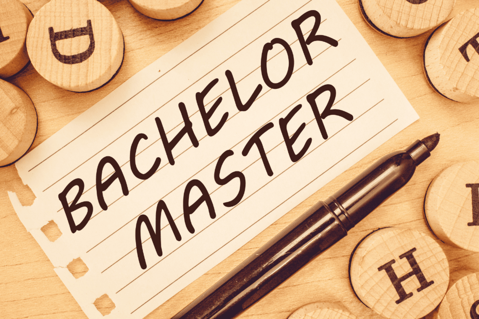 Eine Notizkarte mit der Aufschrift „BACHELOR MASTER“, die neben einem schwarzen Stift liegt und von Holzbuchstaben umgeben ist.