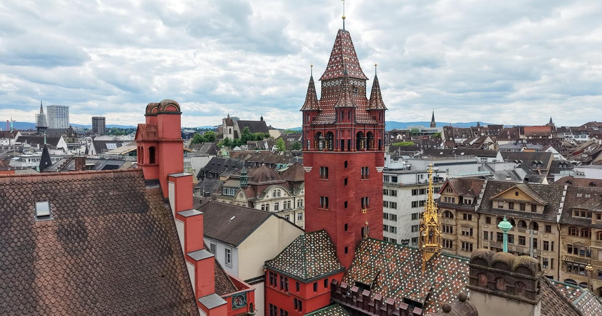 Ein Blick auf die Basler Altstadt mit dem Roten Turm und dem Ziegeldach des historischen Rathauses, umgeben von traditionellen Gebäuden unter einem bewölkten Himmel.